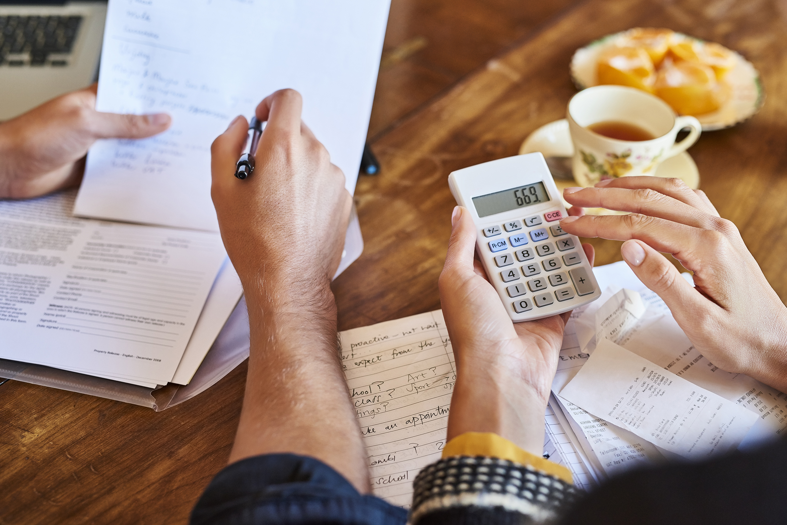 Cropped image of couple doing paperwork with a calculator. Young male and female partners are calculating expenses. They are sitting at breakfast table.